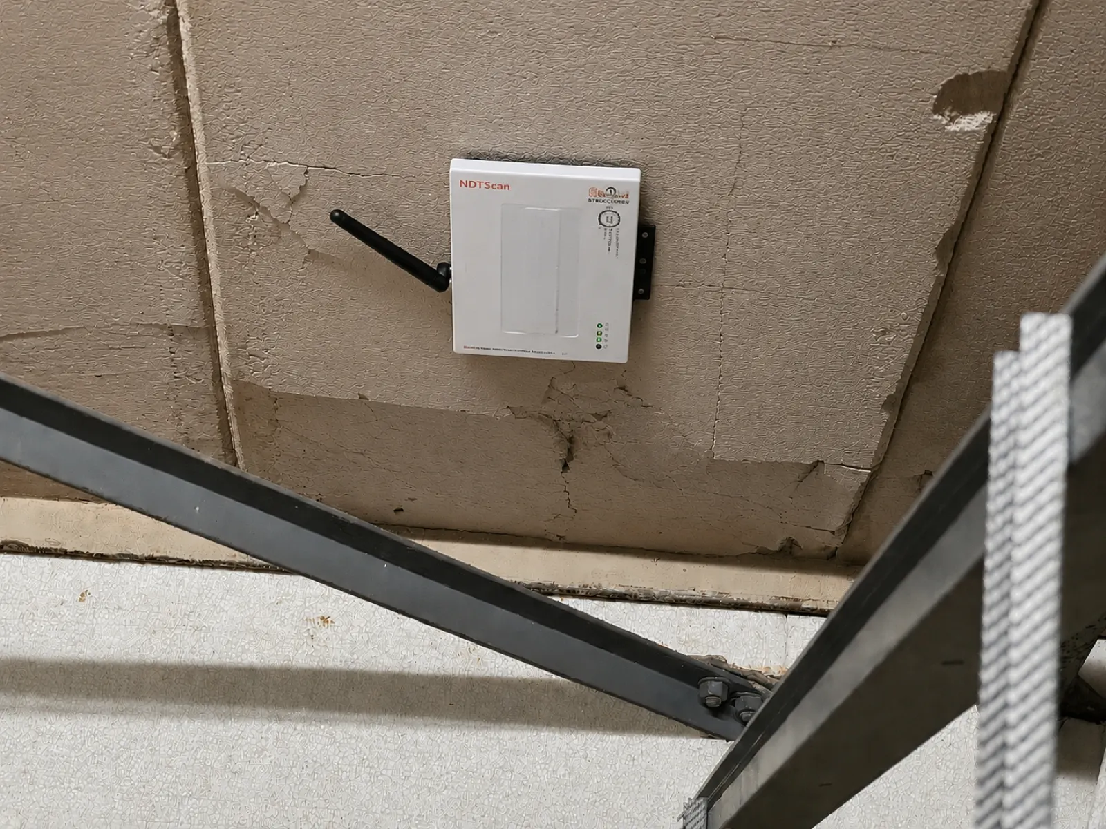 A monitoring device fixed to the underside of a RAAC roof plank